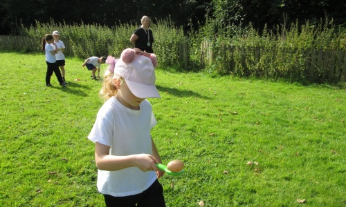 Child with baseball cap with bear ears doing egg and spoon race