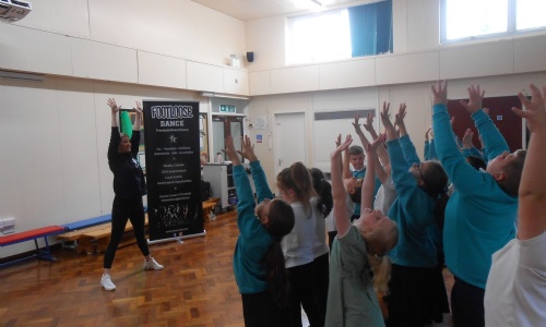 Children facing dance teacher and copying raised arms