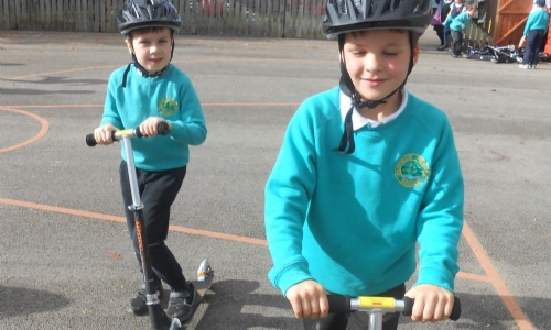 Two happy children in crash helmets on scooters in the playground
